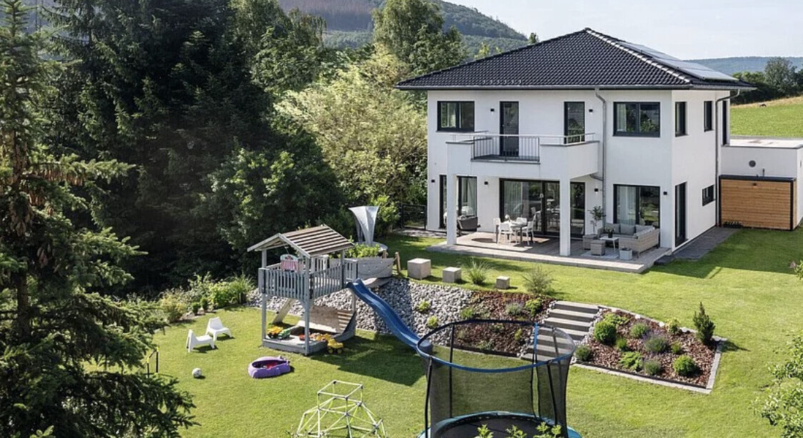 Modernes zweistöckiges weißes Haus mit Garten, Terrasse und Spielbereich im Freien.