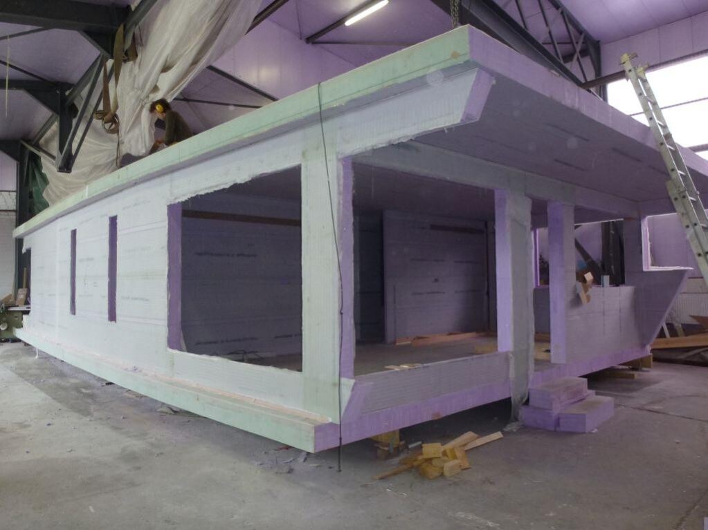 Großes, hellgrünes Holzbauprojekt in einer Werkstatt, Fensteröffnungen, Arbeiter oben.