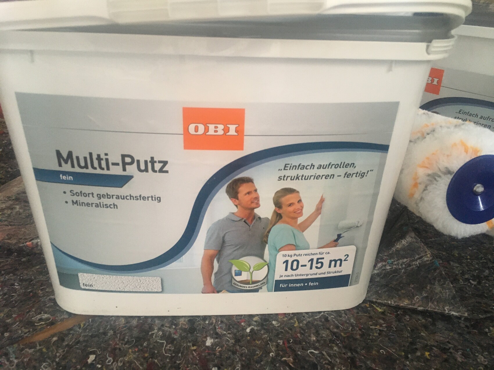Weißer Eimer mit OBI Multi-Putz fein; Abbildung von Mann und Frau mit Malerrolle.