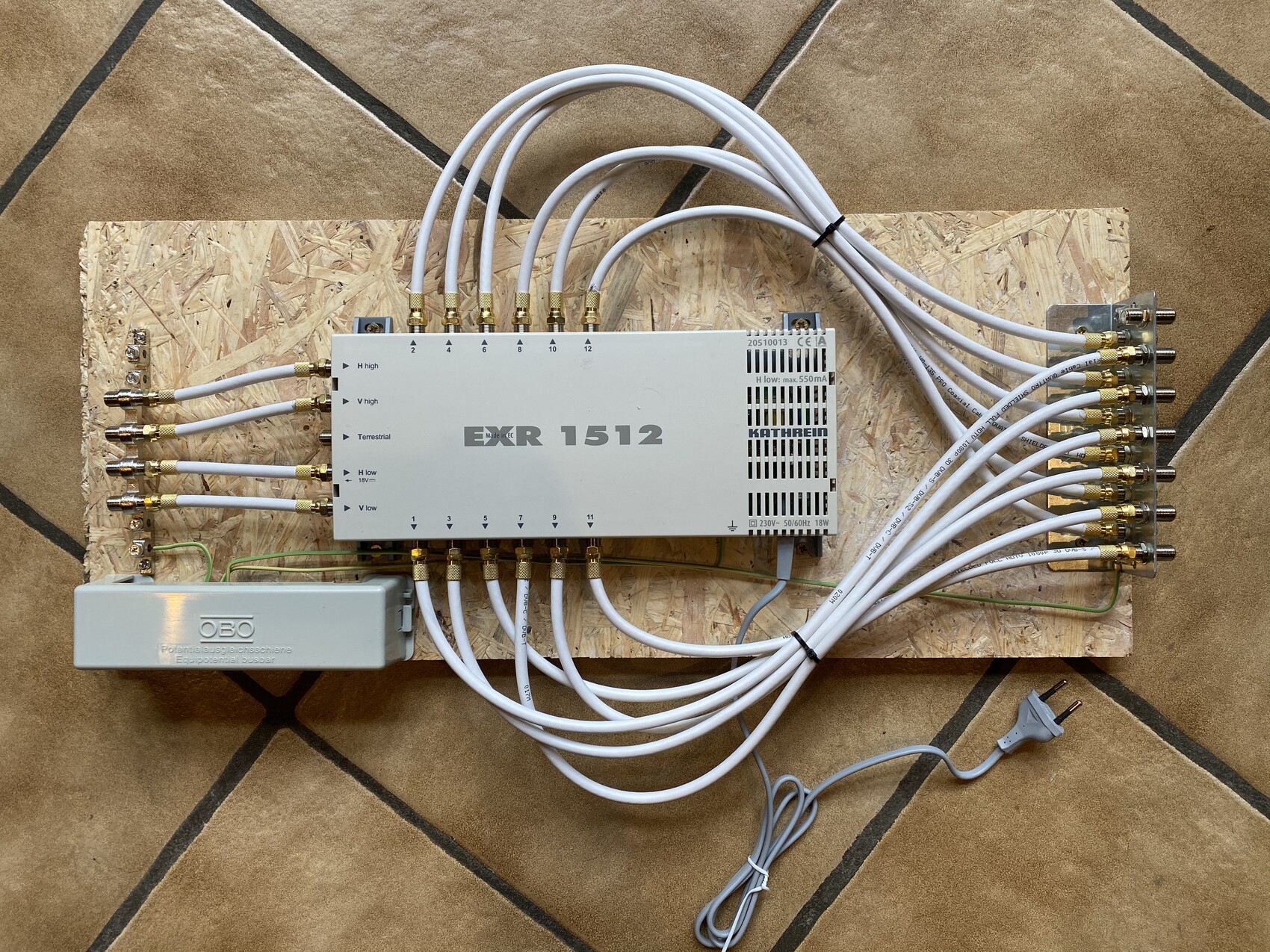 Großer Metallverteiler EMR 1512 mit vielen weißen Koaxialkabeln auf einer Holzplatte.