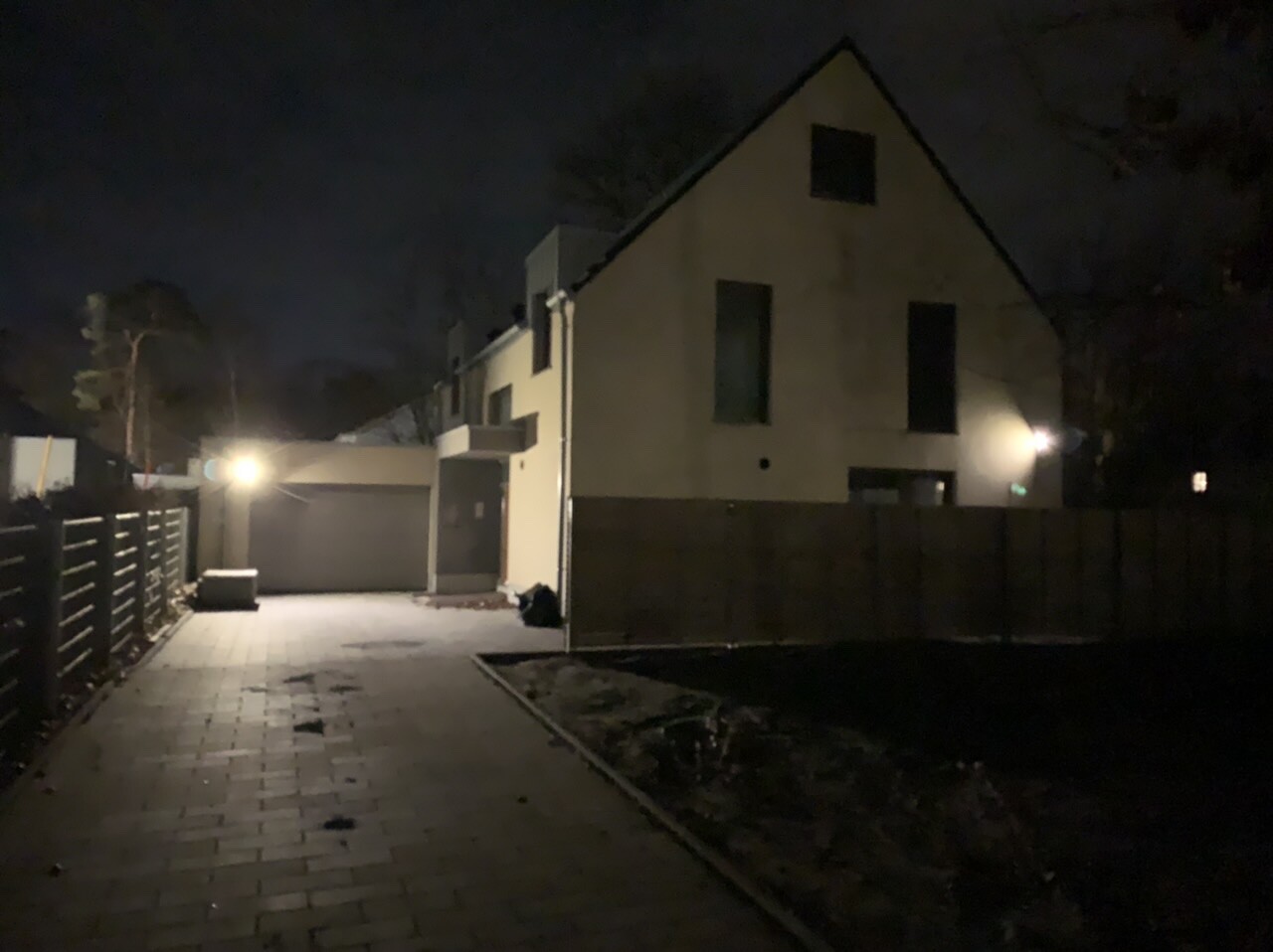 Nachtaufnahme eines modernen Hauses mit Satteldach, beleuchteter Eingang und Garage.