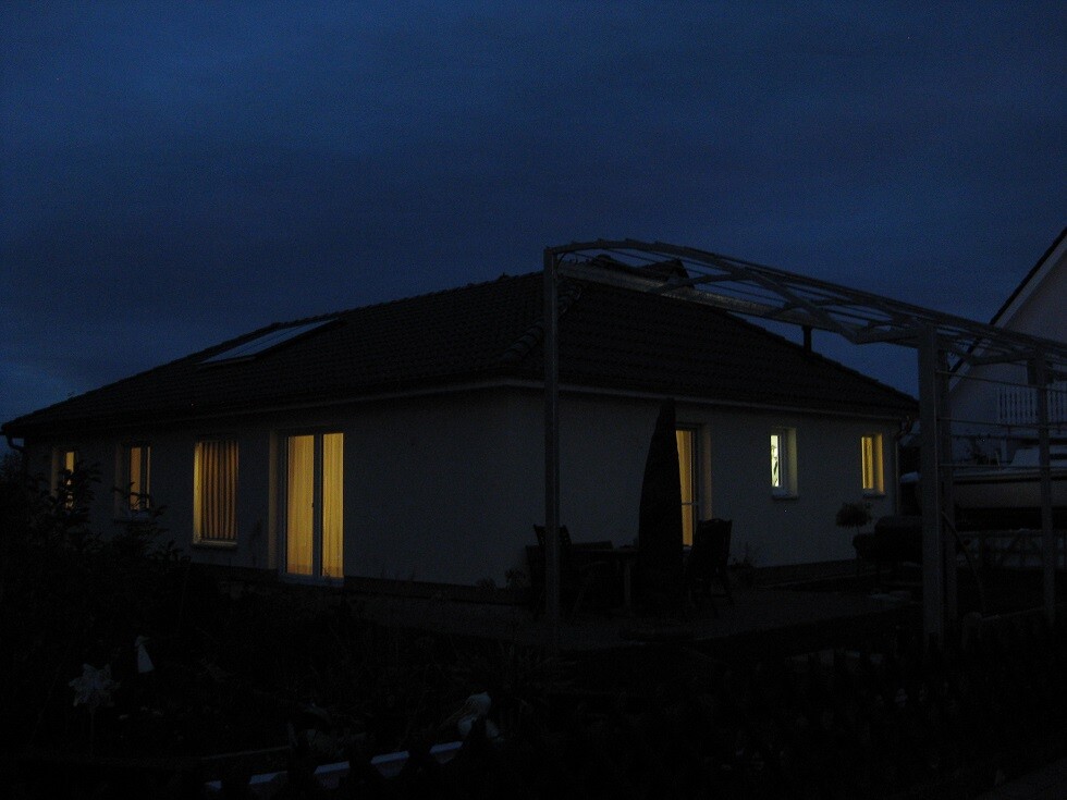 Nachtaufnahme eines Hauses mit beleuchteten Fenstern und Terrasse