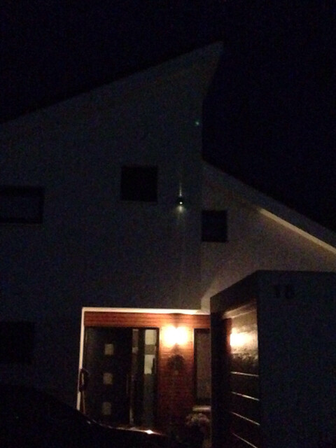 Nachtaufnahme eines modernen Hauses mit beleuchteter Eingangstür und dunklen Fenstern.