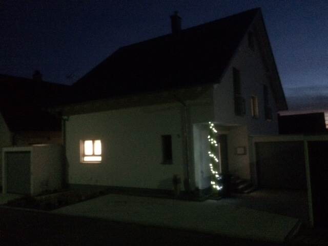 Nachtaufnahme eines Hauses mit beleuchtetem Eingang und Fenster