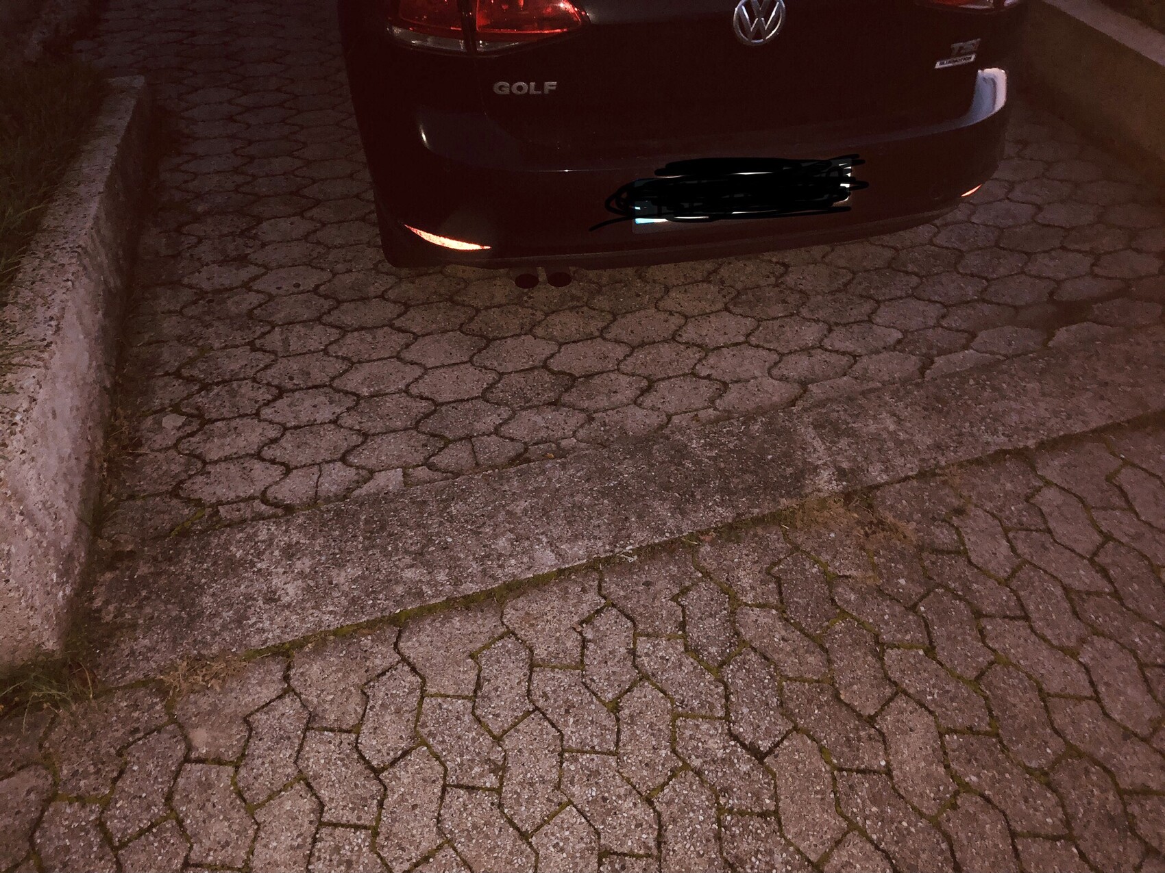 Rückansicht eines schwarzen VW Golf, geparkter PKW auf gepflastertem Parkplatz bei Nacht
