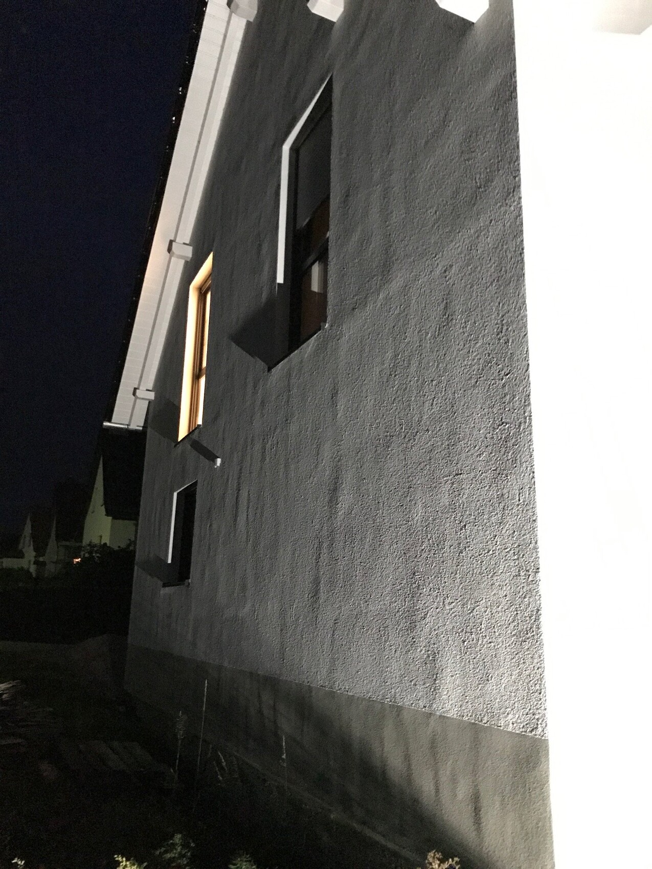 Nachtaufnahme einer grauen Hausaußenwand mit Fenstern bei Nacht