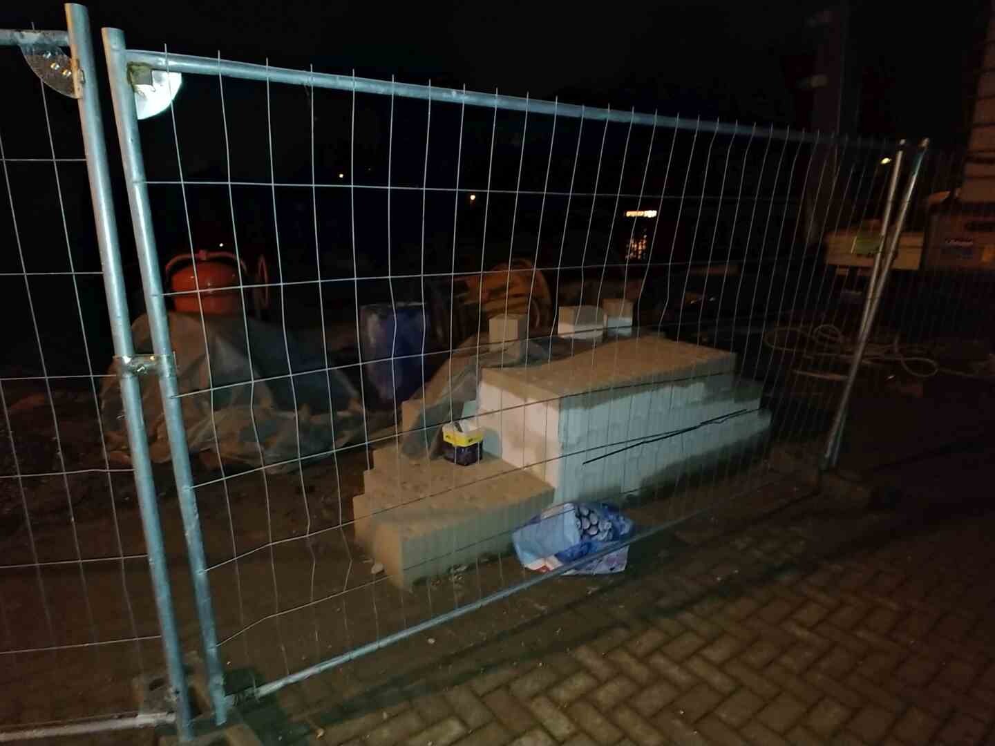 Nachtaufnahme einer Baustelle mit Metallzaun, Baumaterialien und Fundamentsteinen