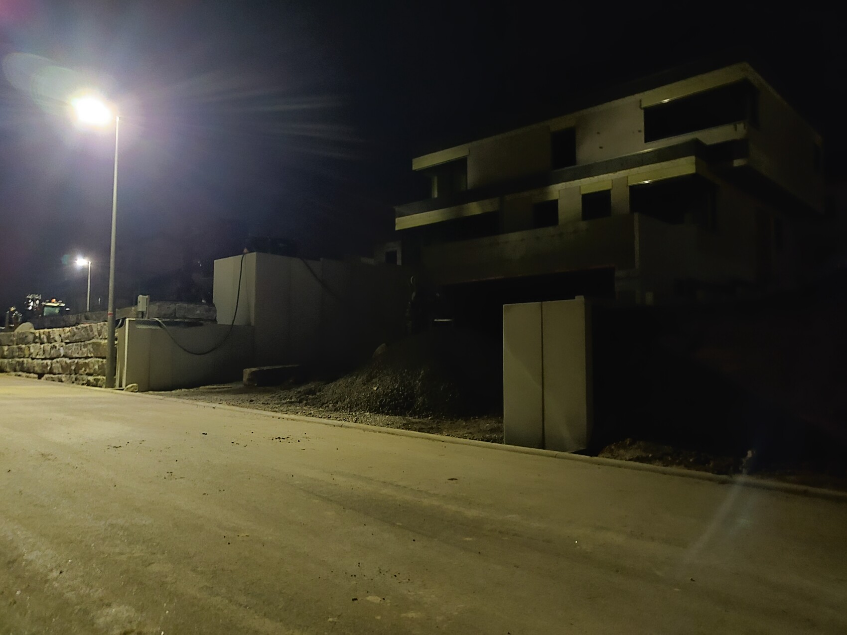 Nachtaufnahme: unvollendeter Betonbau neben der Straße, beleuchtet von einer Straßenlaterne.