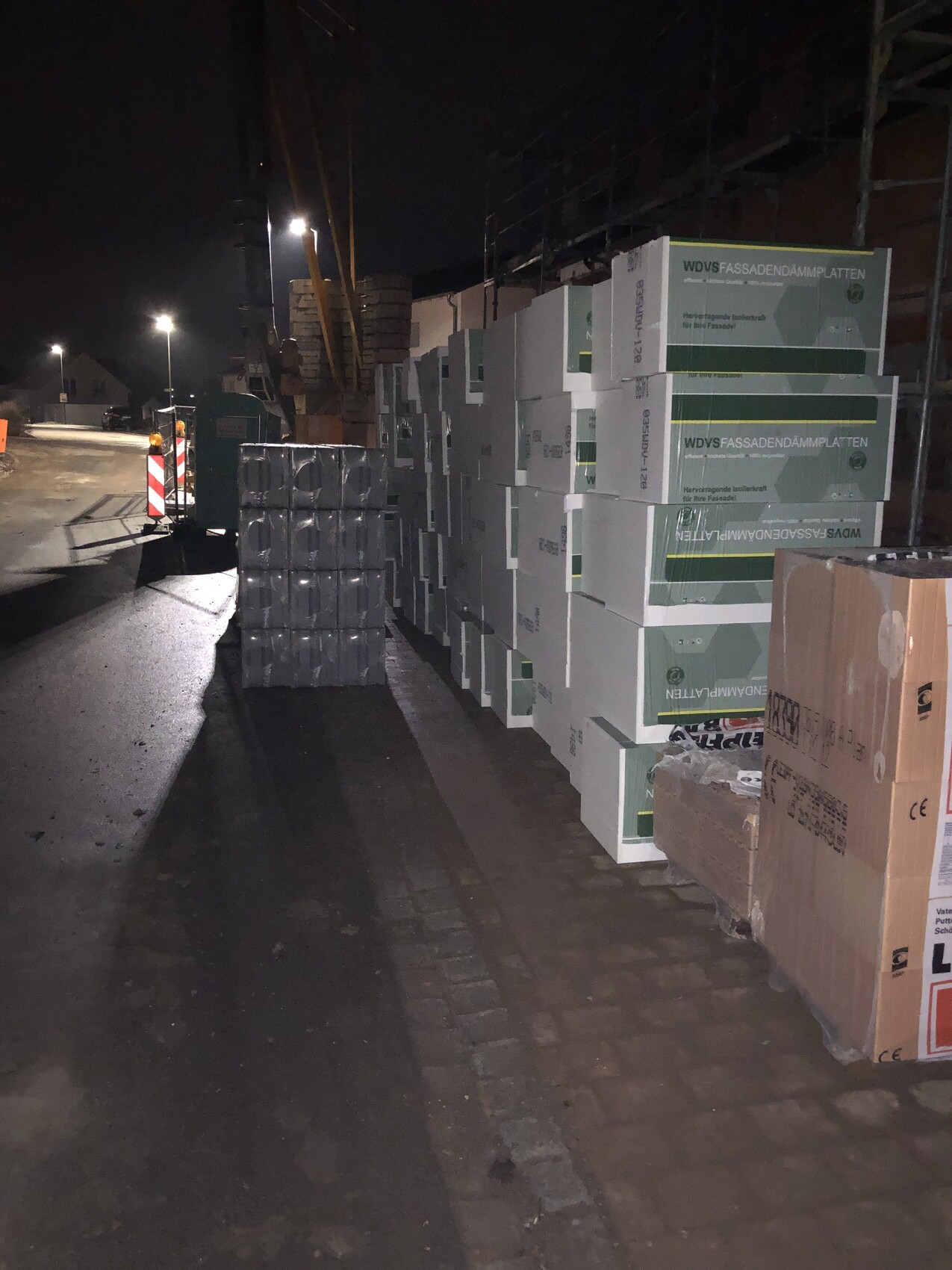 Nächtliche Baustelle mit gestapelten WDVS-Fassadendämmplatten neben einer Straße.