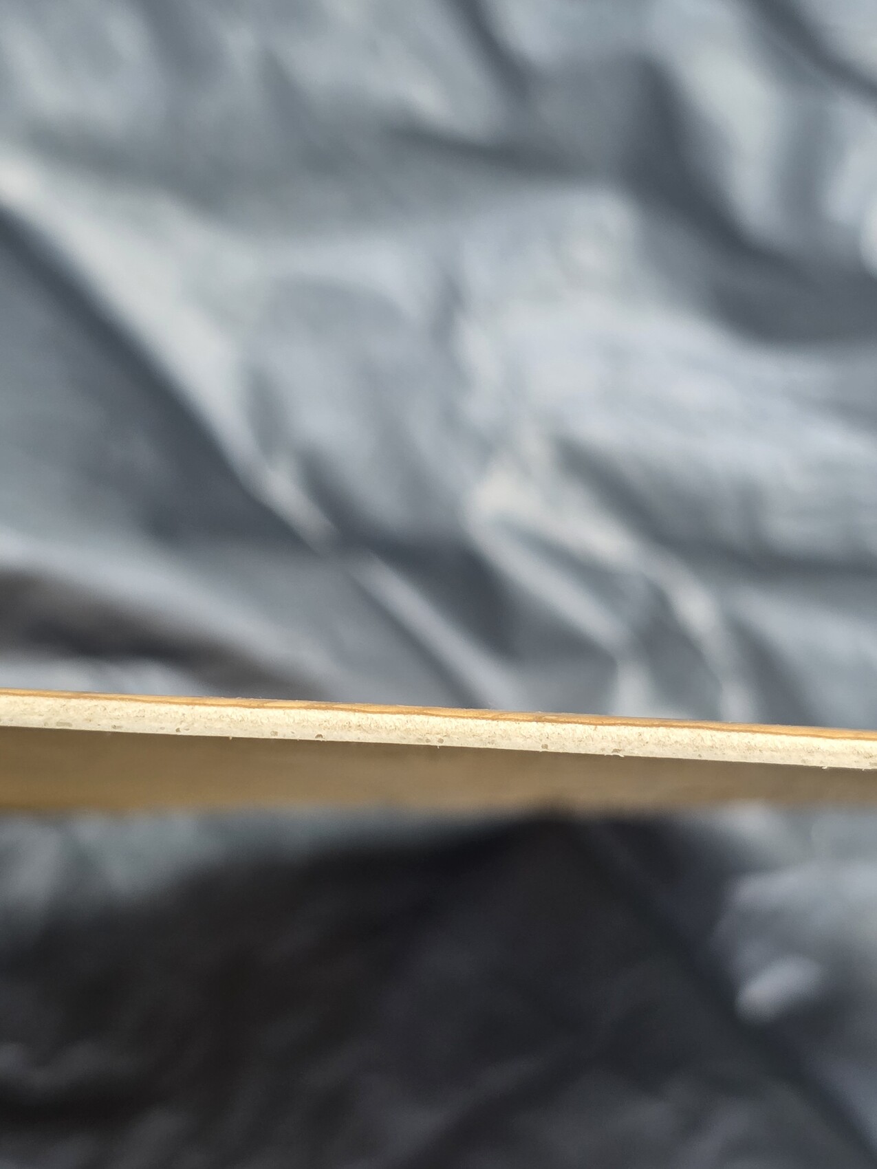 Nahaufnahme einer goldfarbenen Kante eines flachen Gegenstands vor grauem, unscharfem Hintergrund