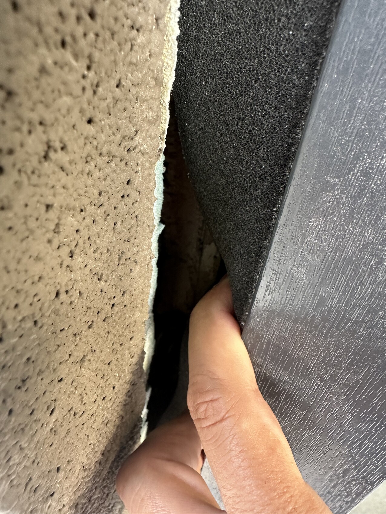 Hand drückt schwarzen Schaumstoff-Dichtungsstreifen in Spalt zwischen Wand und Türrahmen.