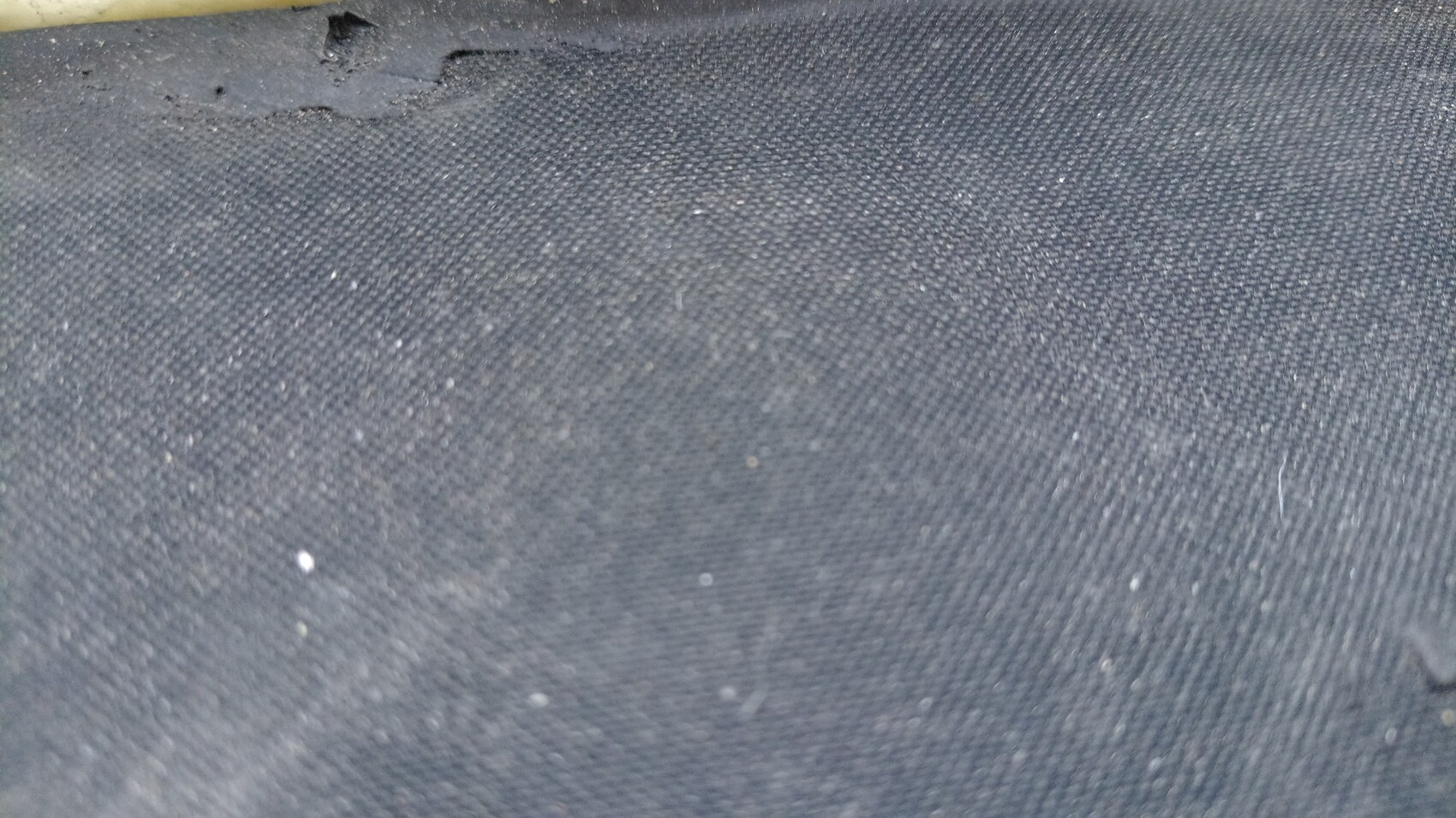 Dunkler Jeansstoff Nahaufnahme mit Staubkörnern; oben links sichtbar eine helle Stange.