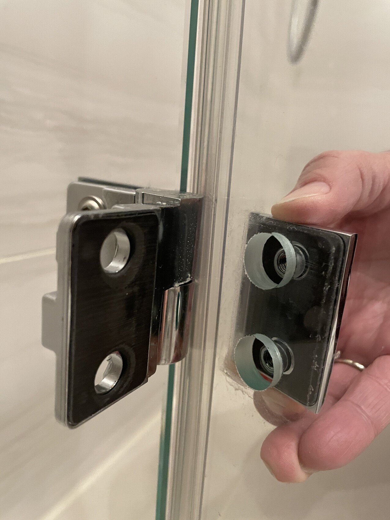 Nahaufnahme eines Glas-Duschtür-Scharniers mit Metallbeschlägen, Hand hält Bauteil.