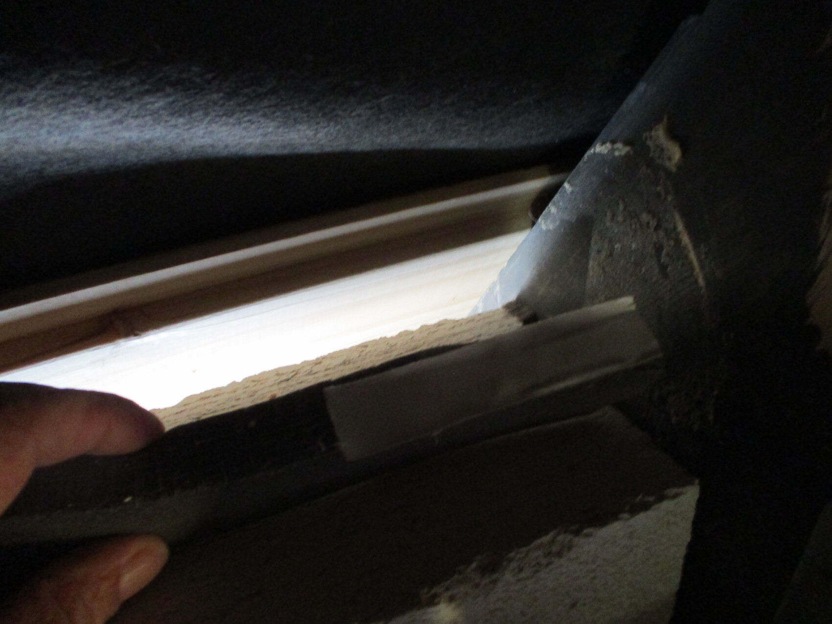 Nahaufnahme einer Hand, die einen Spachtel an einem Fensterrahmen mit Putzreste hält.