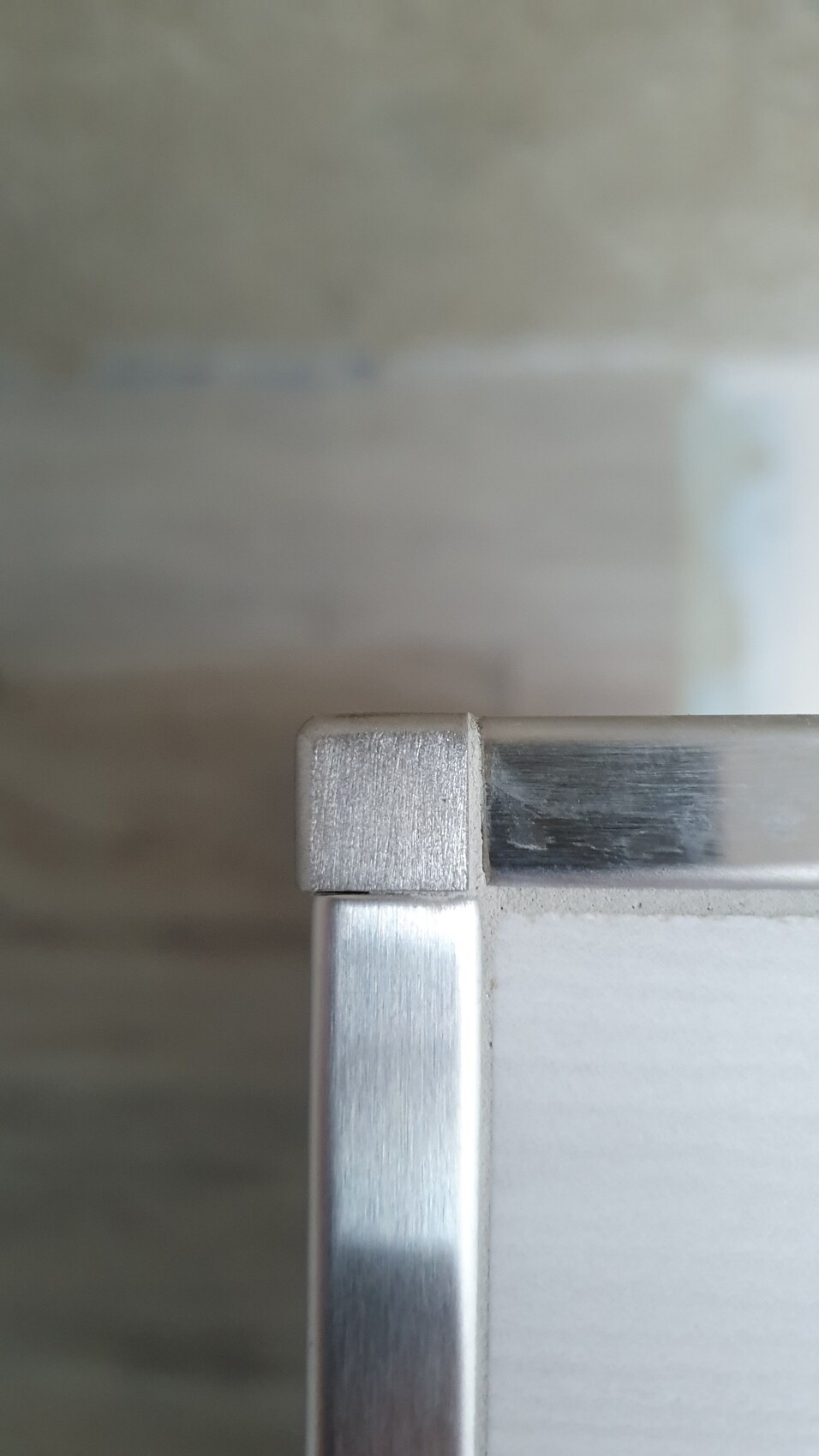 Nahaufnahme einer silbernen Metallrahmenkante mit weißem Paneel, Ecke sichtbar.