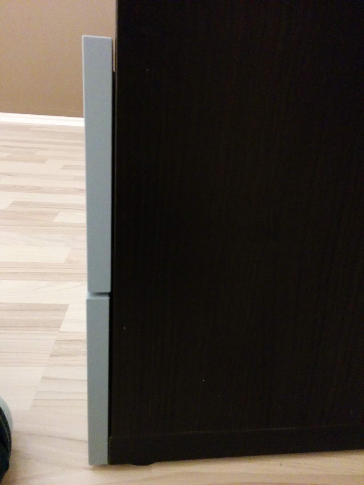 Nahaufnahme einer dunklen Möbelfront mit grauer Metallkante links, Holzboden im Hintergrund