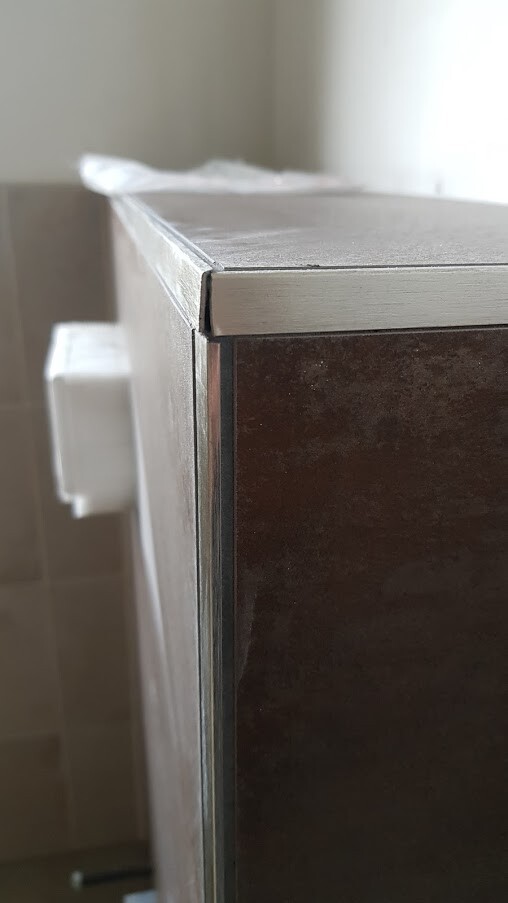 Nahaufnahme der Ecke eines dunklen Holzschranks mit Metallkante; weißer Türknopf sichtbar.