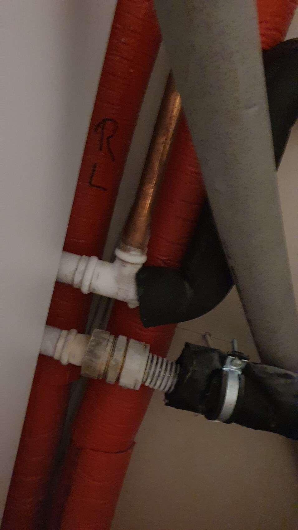 Sanitärrohre hinter einer Wand: rote Isolierrohre, Kupfer- und Kunststoffverbindungen.