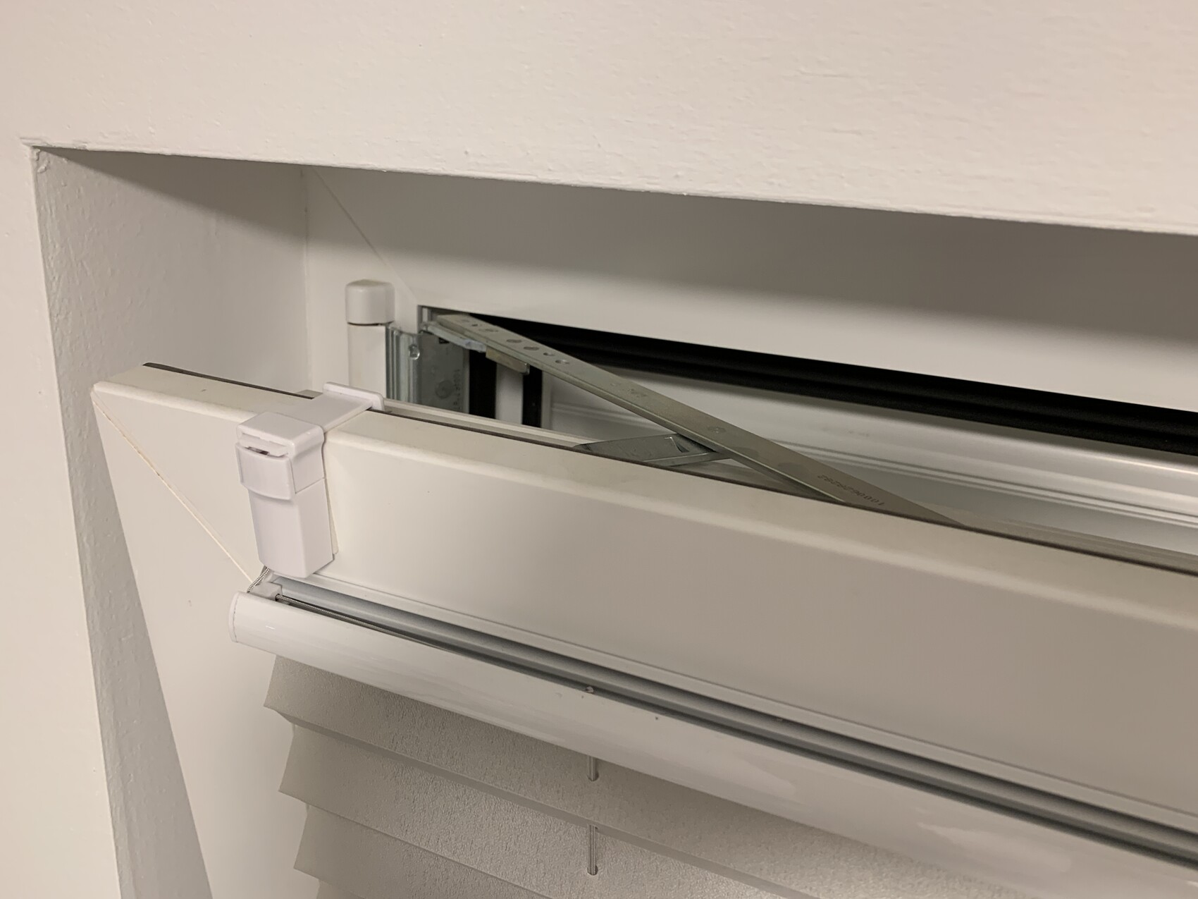 Nahaufnahme einer weißen Innenjalousie mit geöffnetem Rollladen-Mechanismus und Metallstreifen