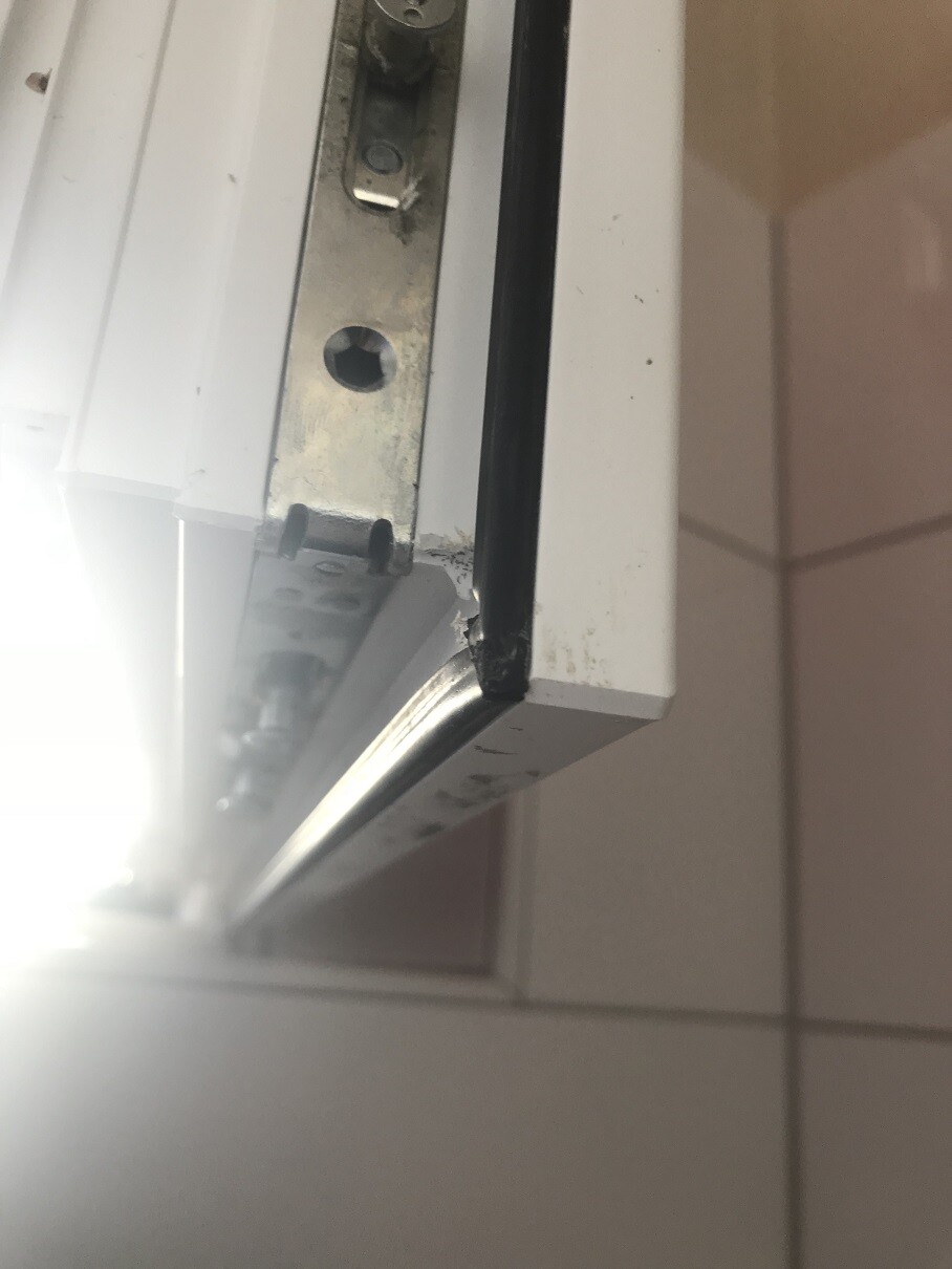 Nahaufnahme einer weißen Türkante mit Metallteil und Schrauben am Rahmen