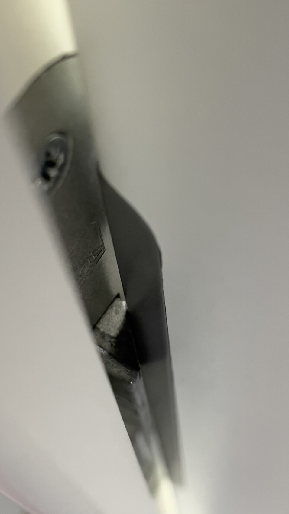 Nahaufnahme einer dunklen Metallkante mit Schraubenkopf, seitlich aufgenommen.
