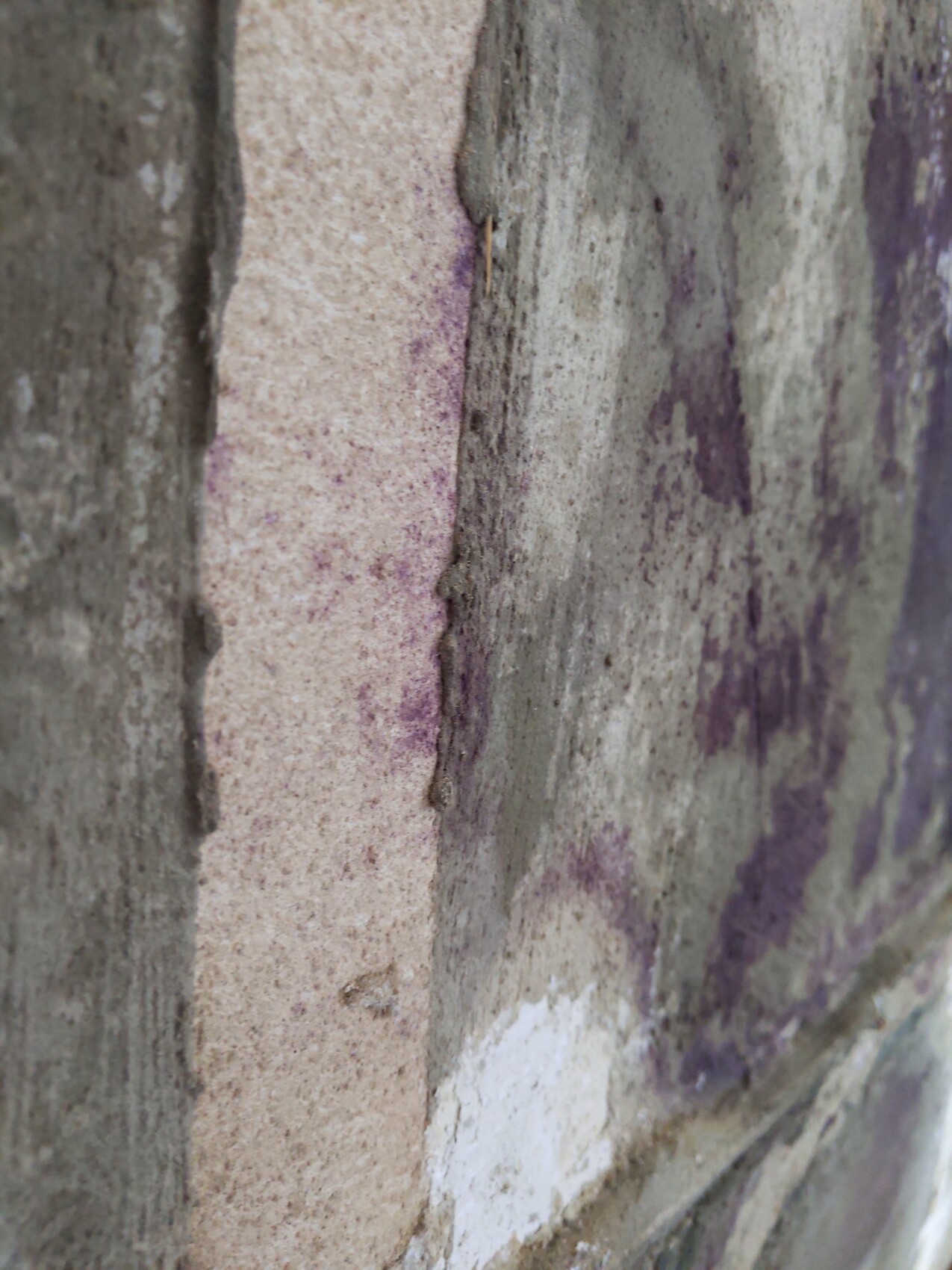 Nahaufnahme einer rauen Steinwand mit grauen Steinen und violetten Flecken.
