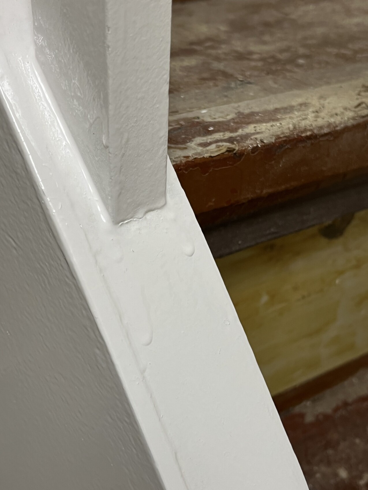 Nahaufnahme einer weißen Treppenkante neben braunen Holzstufen mit abgeplatzter Lackierung.
