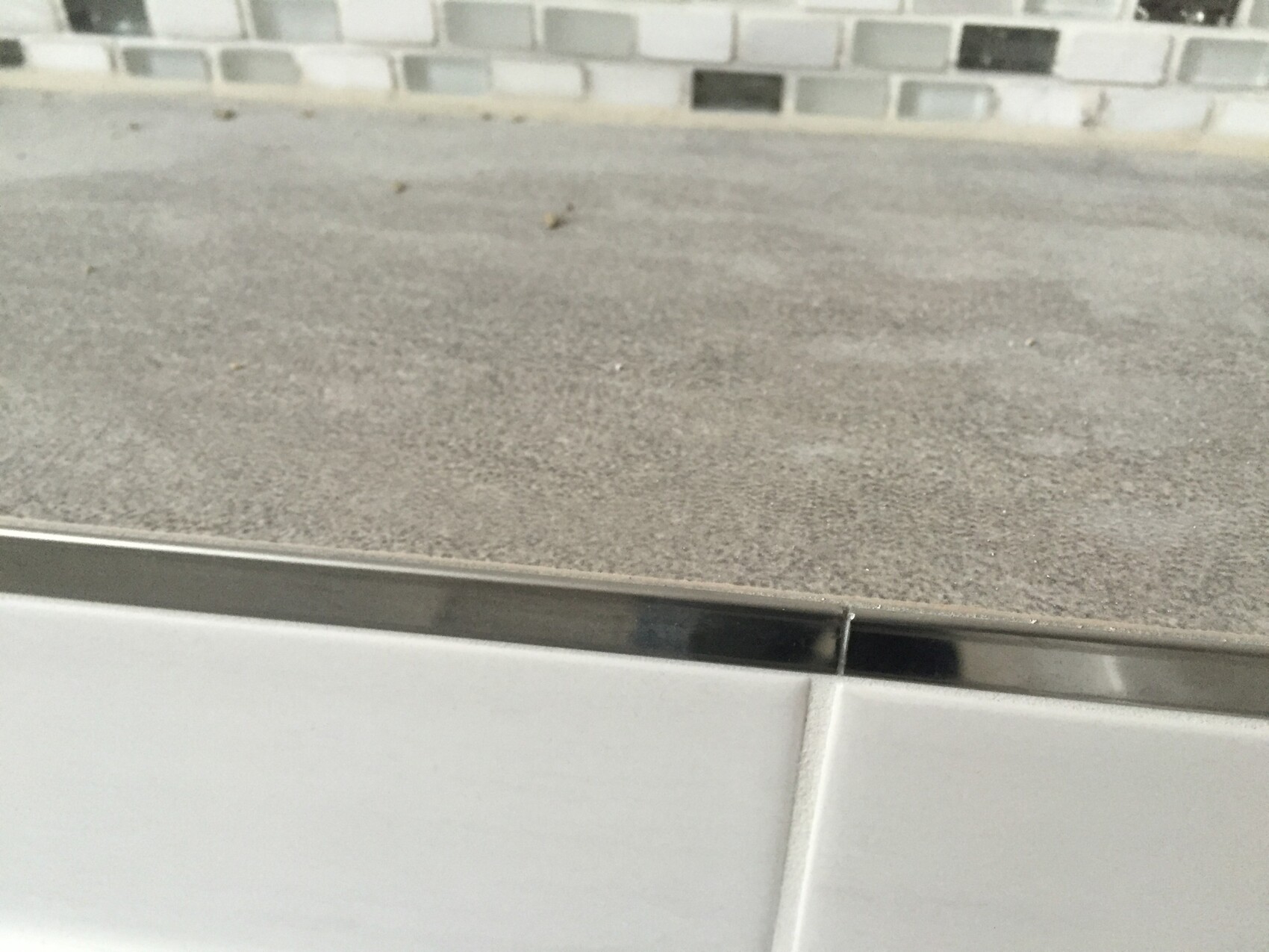 Nahaufnahme einer Küchenarbeitsplatte mit grauer Fliesenrückwand und Metallrand.