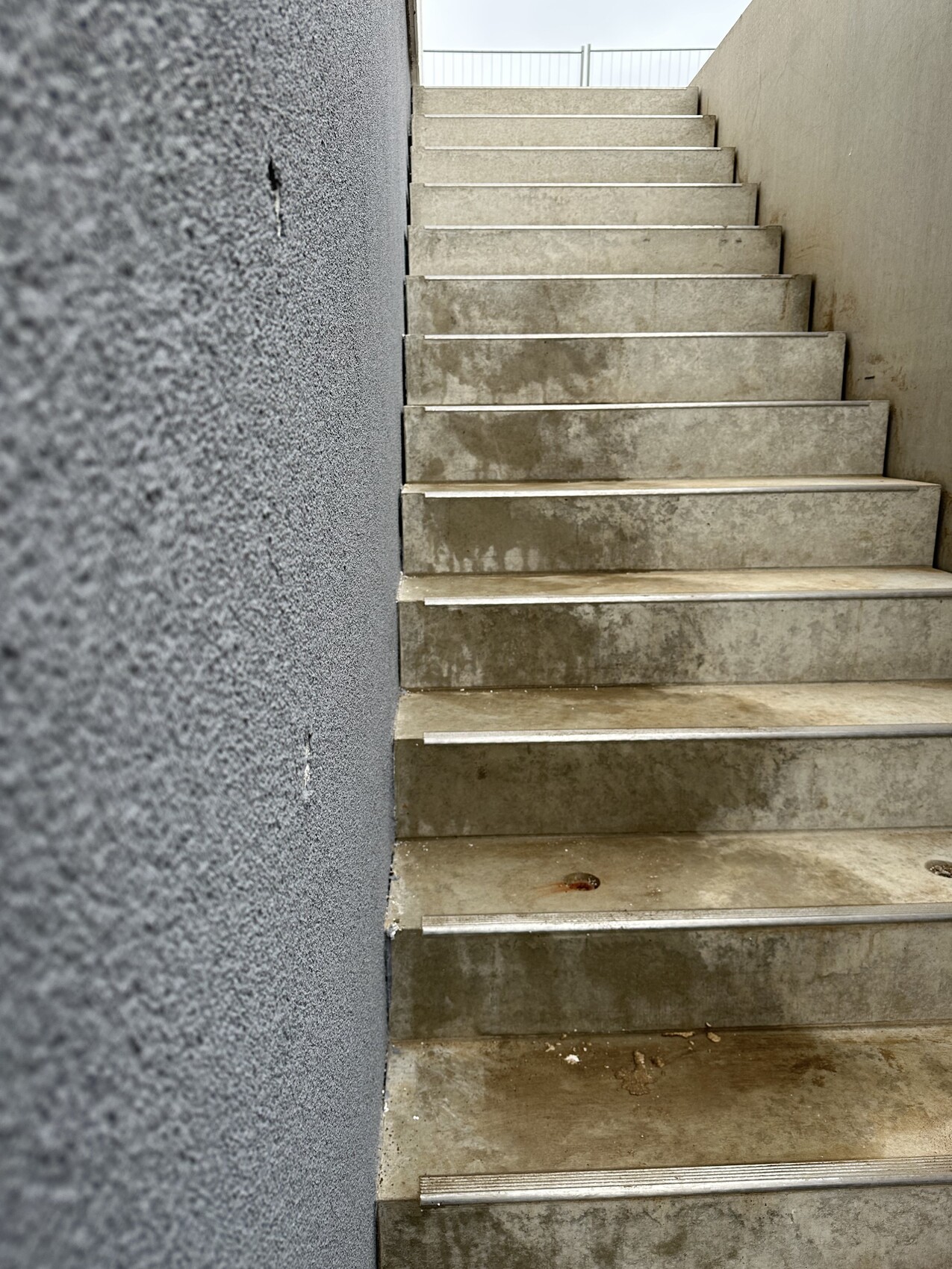 Außentreppen aus Beton zwischen grauen Wänden, feuchte Stufen, Blick nach oben zum Geländer