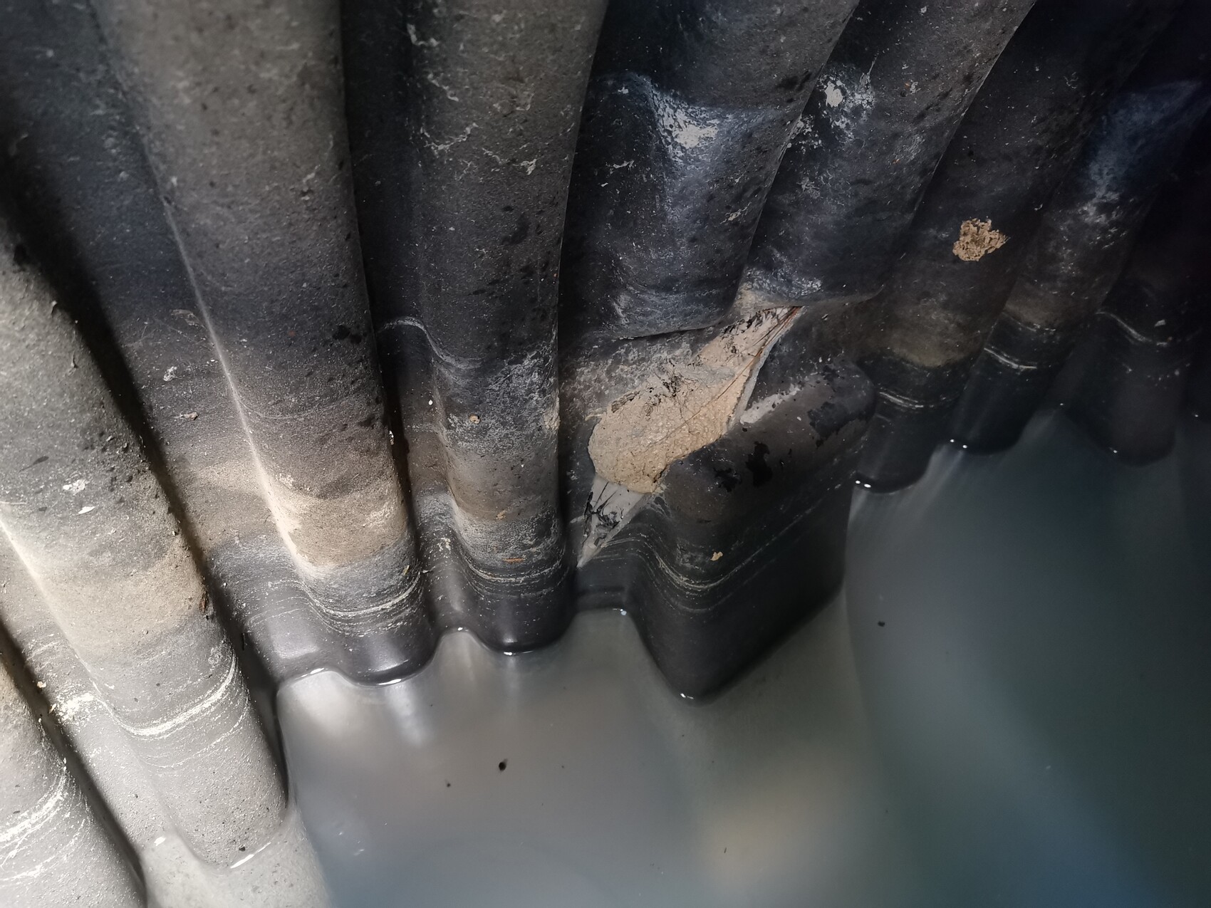 Dunkle, gewölbte Dachziegel mit Abplatzung und Wasser am unteren Rand.