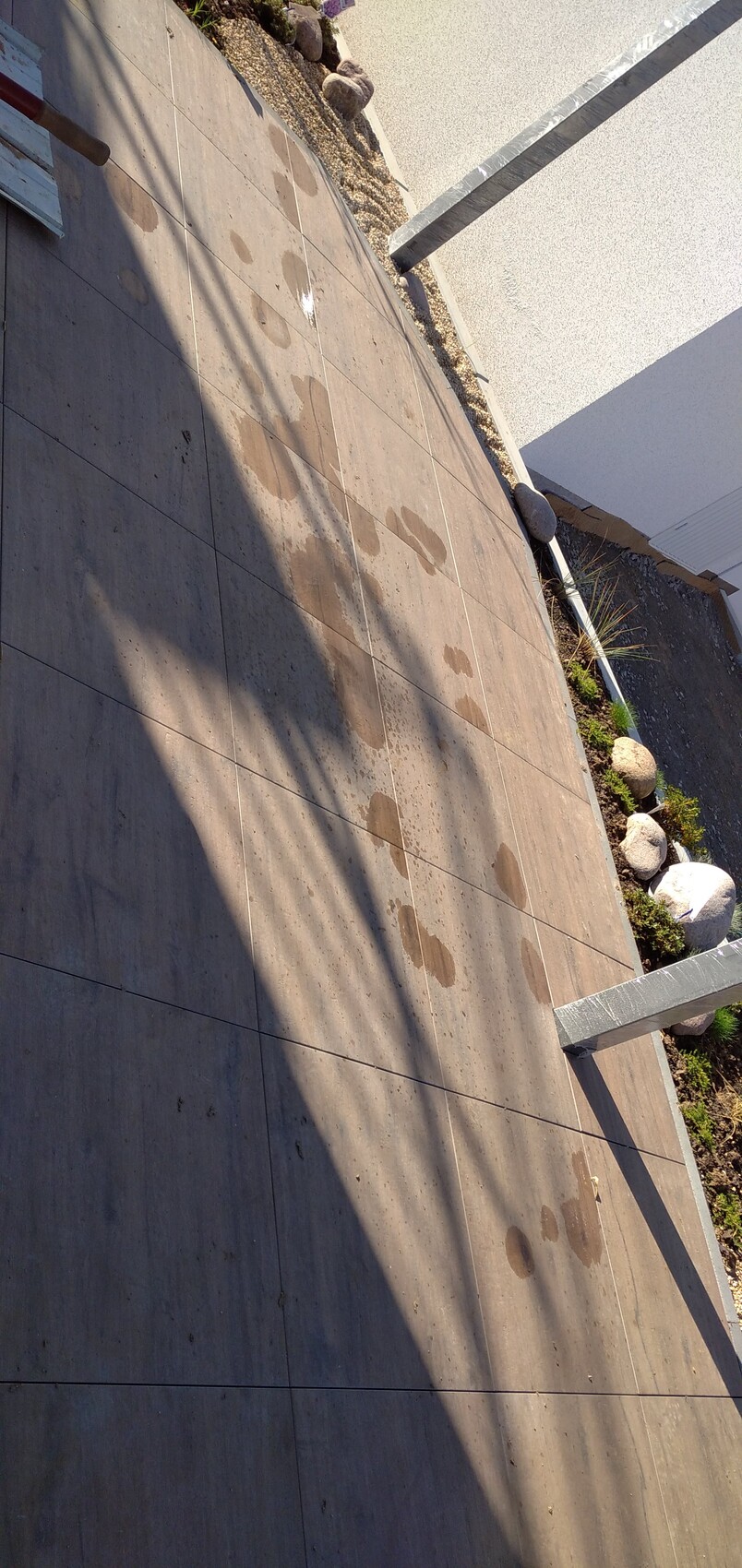 Gepflasterte Terrassenfläche mit nassen Flecken, Schatten und Rand aus Steinen und Pflanzen.