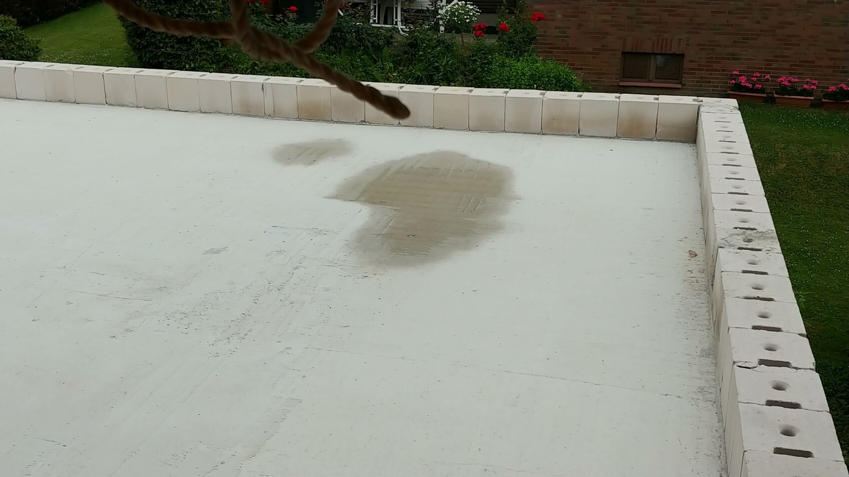 Weisse Flachdach-Terrasse mit nassen Flecken und Garten im Hintergrund