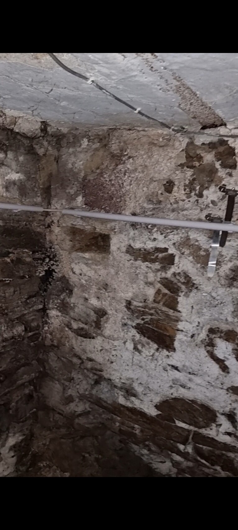 Kellerrraum mit roher Steinwand, Feuchtigkeit, PVC-Rohr und Metallhalterungen.