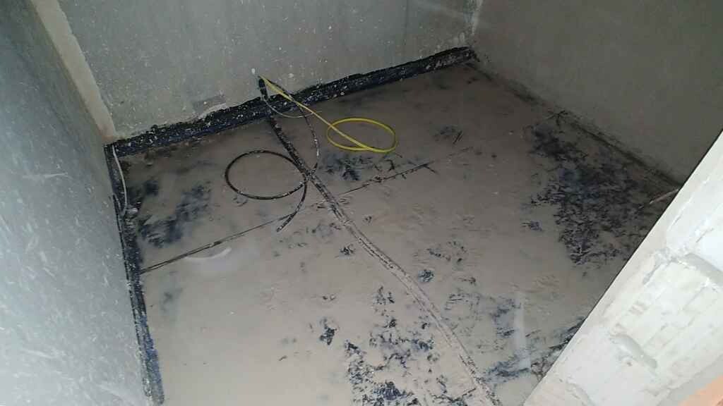 Unbearbeiteter Bauraum mit nassem Betonboden, lose Kabel, rohe Wände und Bauarbeiten.