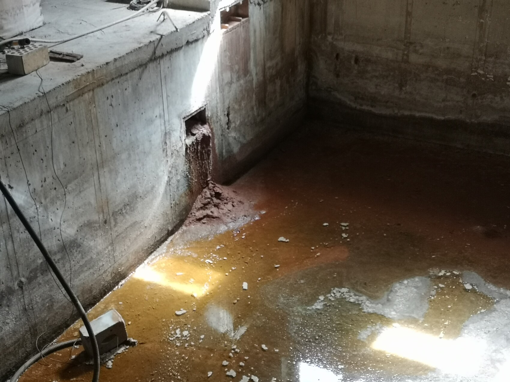 Kellerraum/Baugrube mit brauner Wasserpfütze, feuchte Wand und offenes Wandloch mit Tropfwasser.