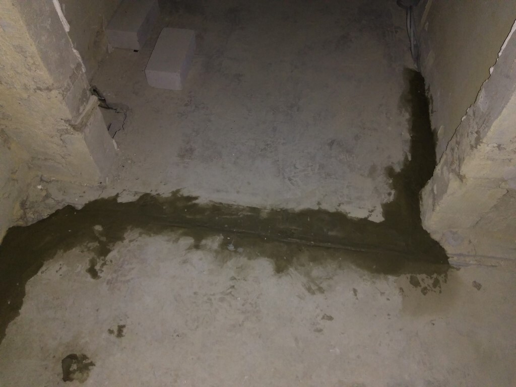 Kellerboden mit feuchter, dunkler Wasserfleckenlinie entlang einer Fuge; rauer Beton, Betonblock