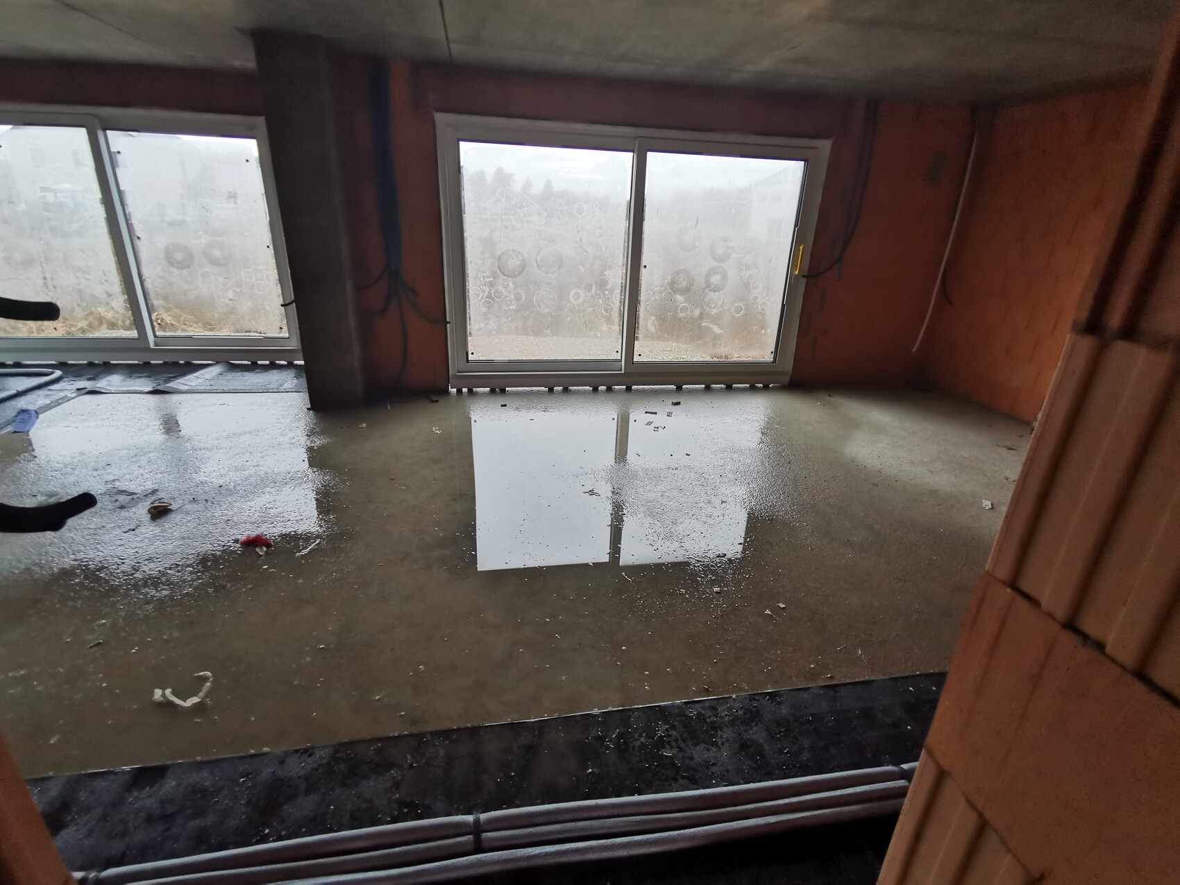 Unbearbeiteter Kellerraum im Rohbau mit großen Fenstern und stehendes Wasser