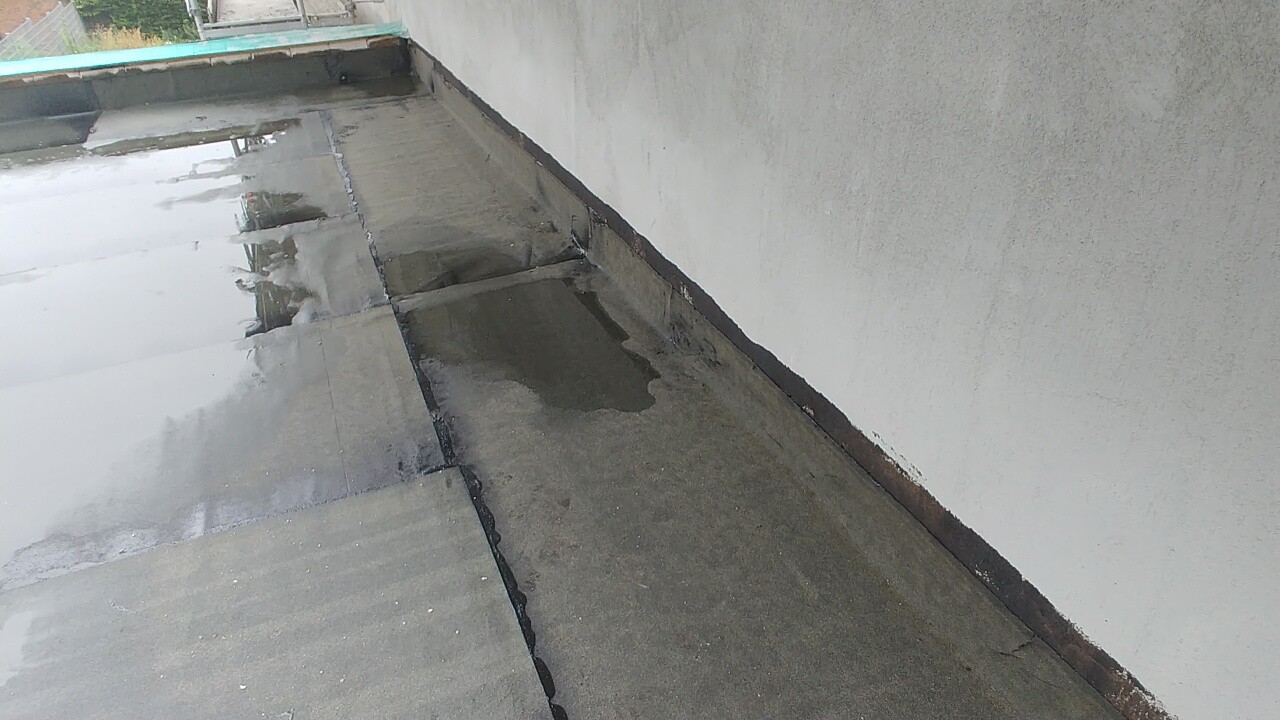 Nasses Flachdach mit Wasserpfützen neben einer Außenwand; sichtbare Dachabdichtung.