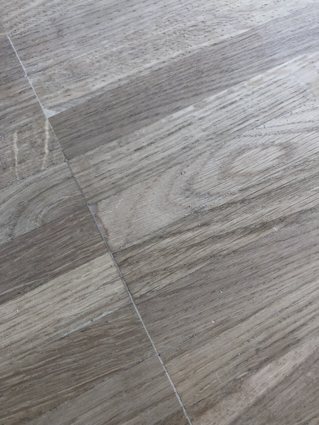 Holzfußboden mit diagonal verlaufender Fuge, sichtbarer Maserung und Staubresten