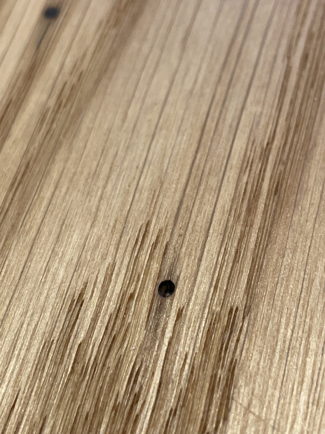 Nahaufnahme einer Holzoberfläche mit feiner Maserung und kleinem schwarzen Loch.