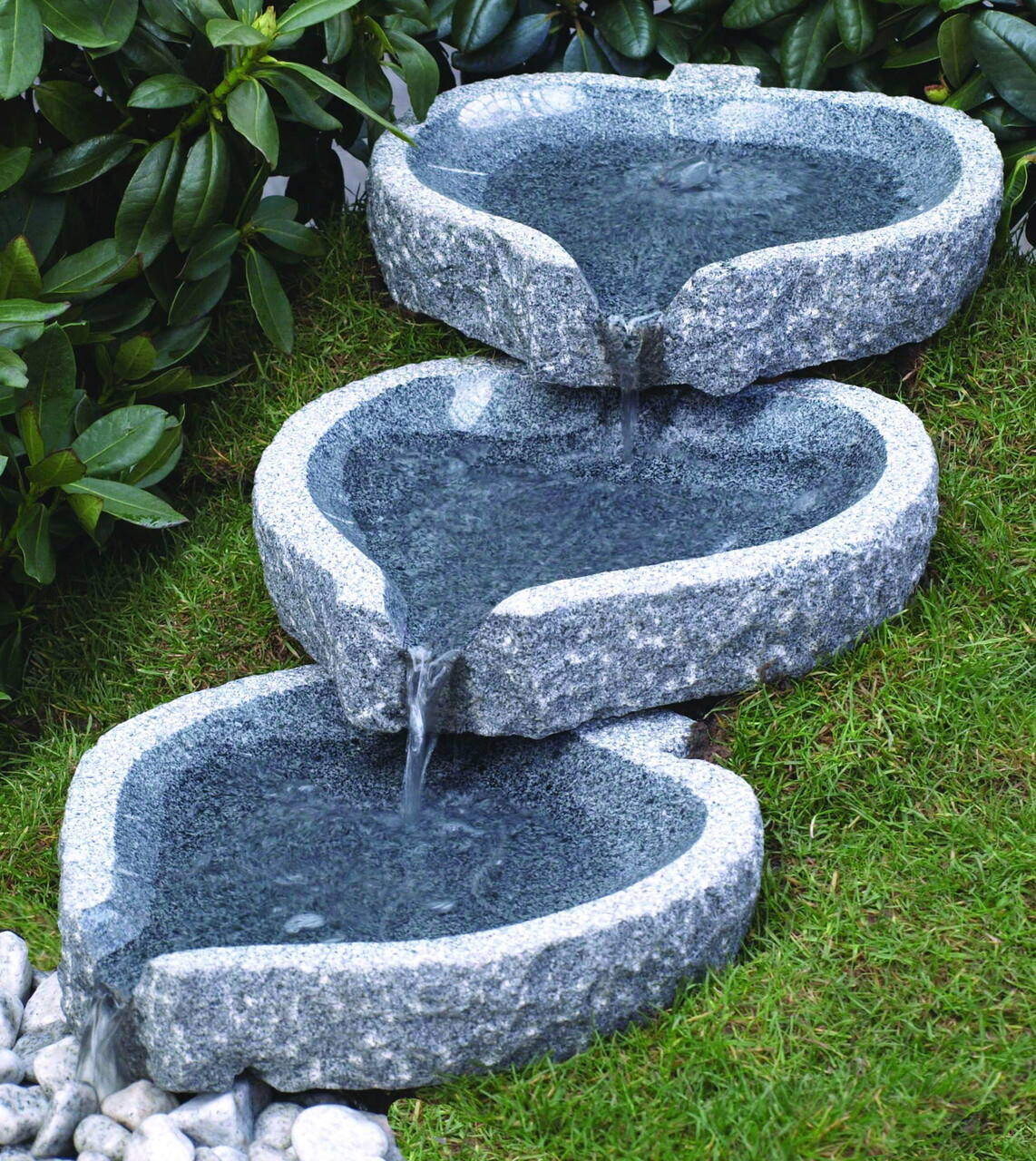 Naturstein-Wasserbrunnen aus drei gestuften Becken im Garten mit Gras und Laub
