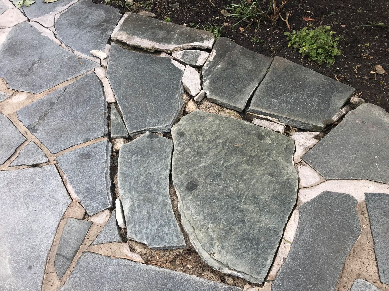 Gartenweg aus unregelmäßigen grauen Steinplatten mit Sandfugen.
