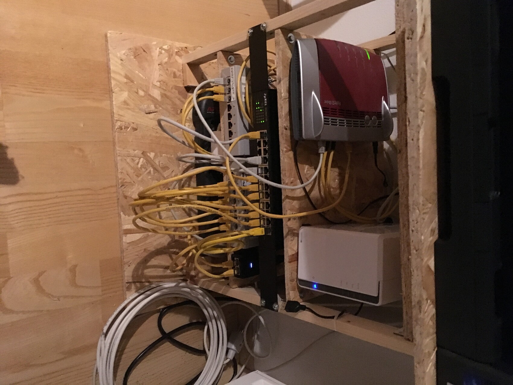 Offenes Wandrack mit Patchpanel, Router und vielen gelben Ethernetkabeln in Bauumgebung