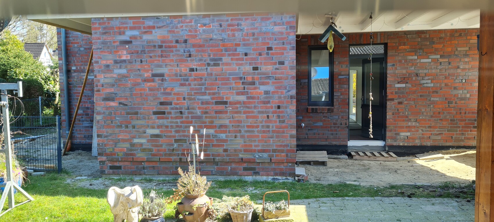 Backsteinfassade eines Hauses im Bau, Tür und Fenster sichtbar, Vordergarten mit Töpfen.
