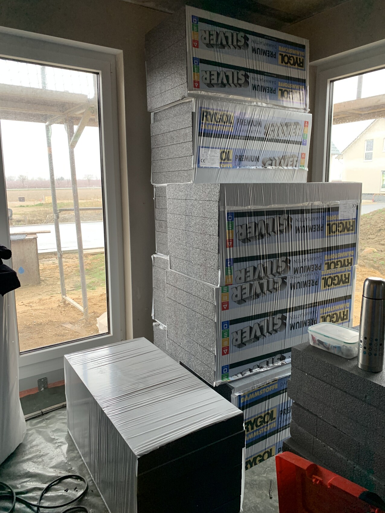 Baustellenraum mit gestapelten Dämmstoffboxen und Styroporplatten vor Fenster.