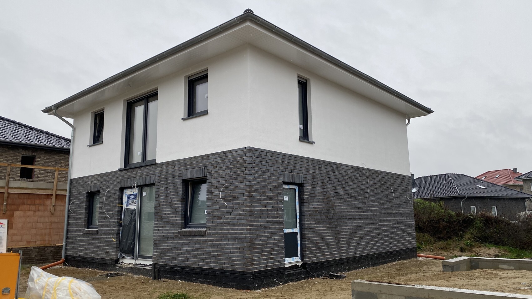 Neubau zweistöckiges Haus im Bau mit dunkler Steinbasis unten und weißer Putzfassade oben.