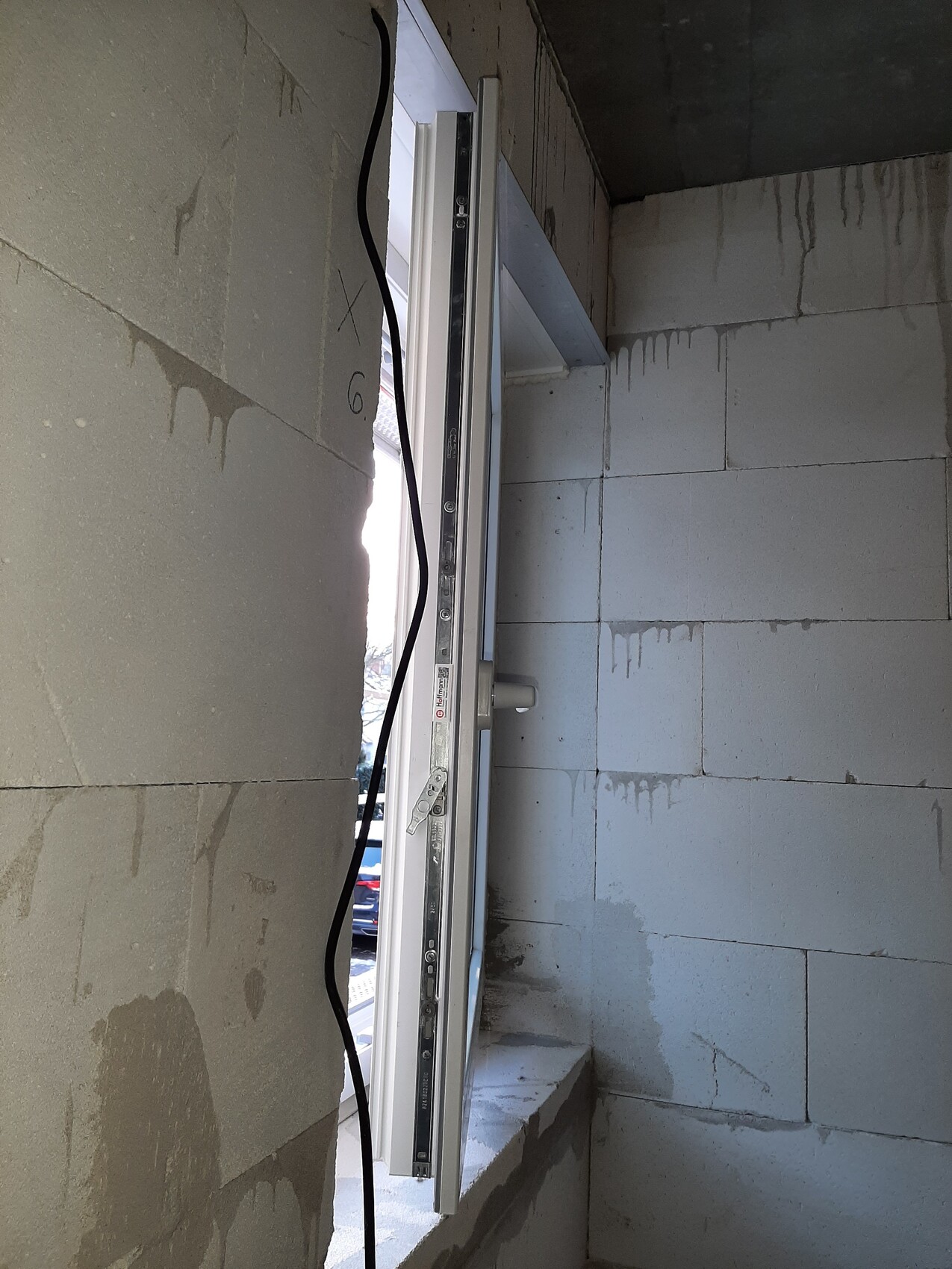 Frisch installierter Fensterrahmen in einer Rohbau-Wand; ein schwarzes Kabel verläuft daneben.