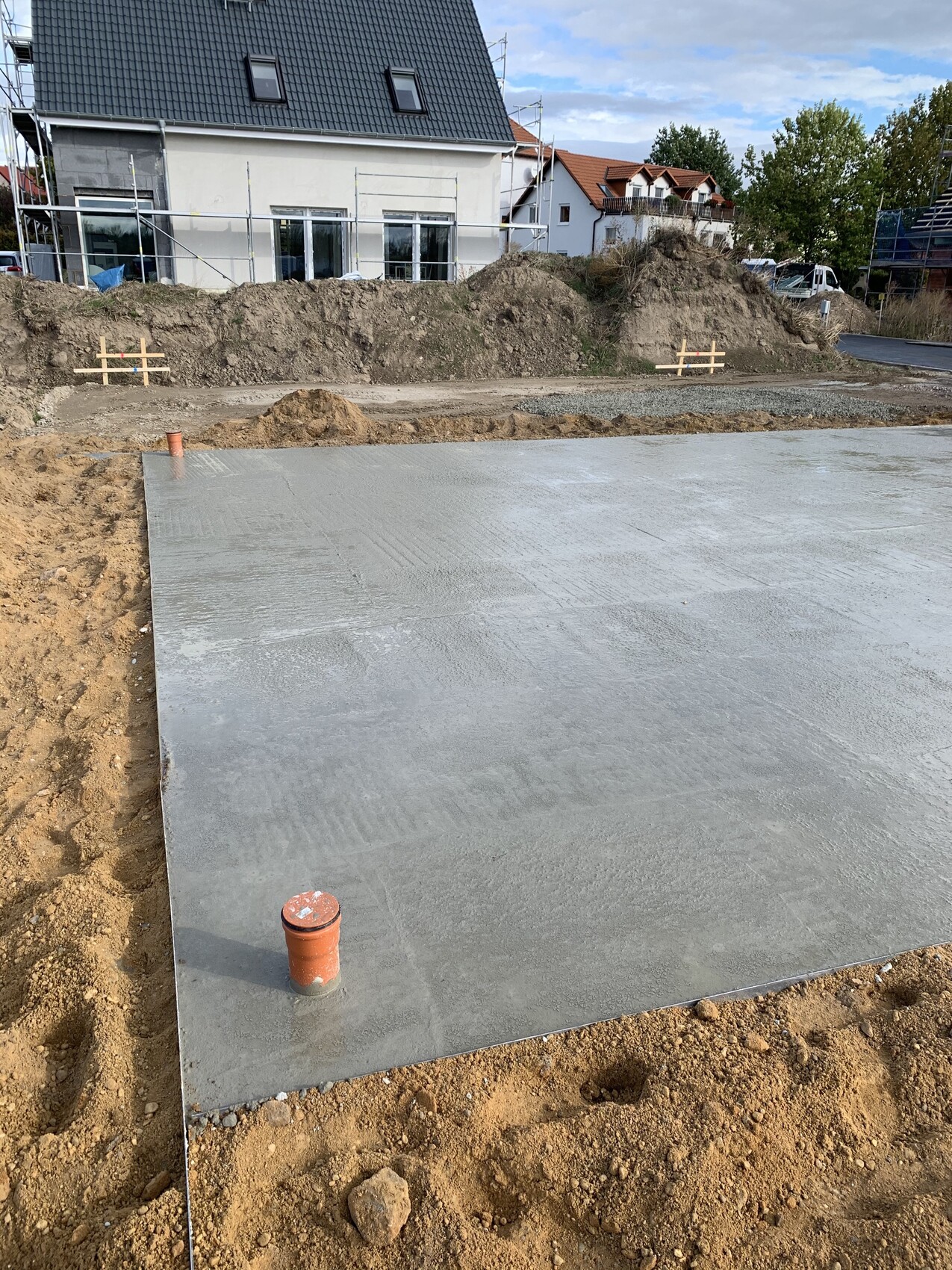 Frisch gegossene Betonplatte auf Baustelle; roter Rohrstutzen am Rand, Gebaeude im Hintergrund.