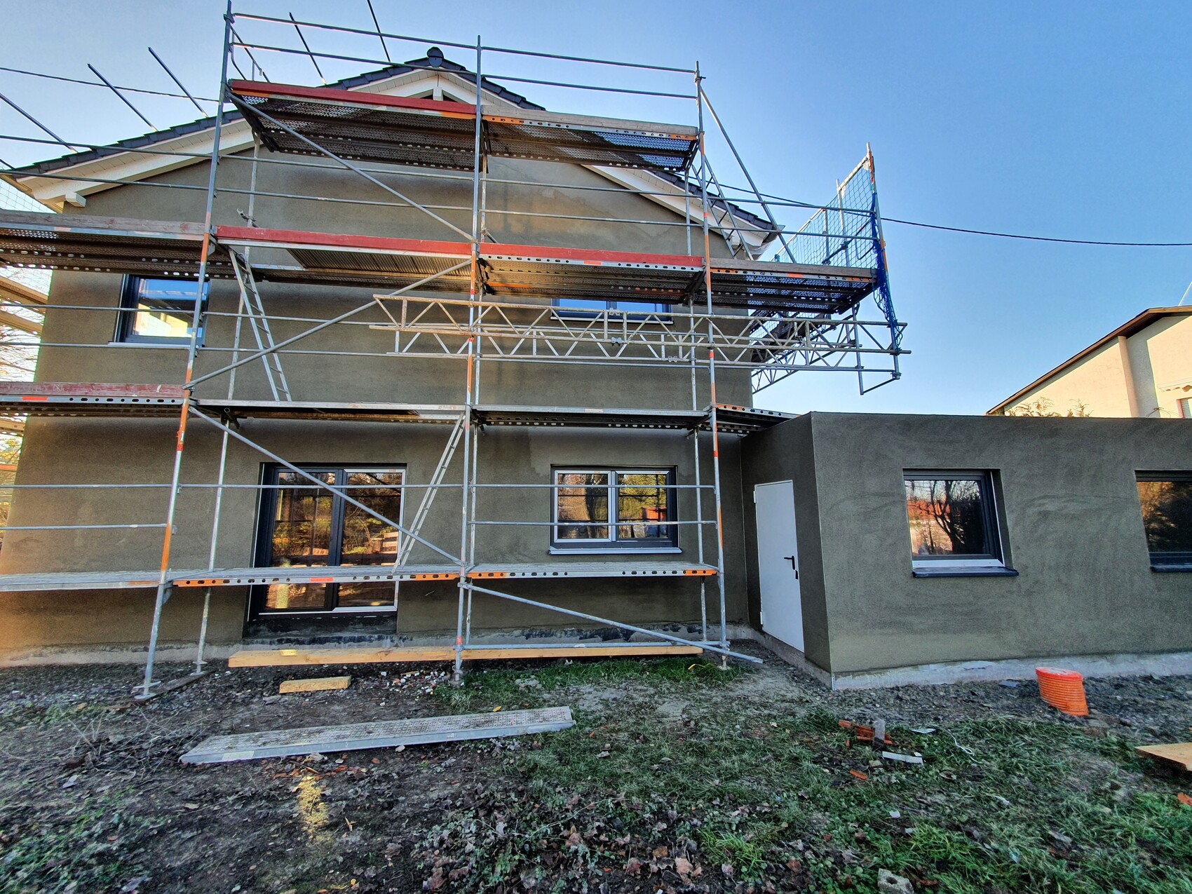Zweistöckiges Haus im Bau mit großem Gerüst, blauen Netzen und laufenden Bauarbeiten.