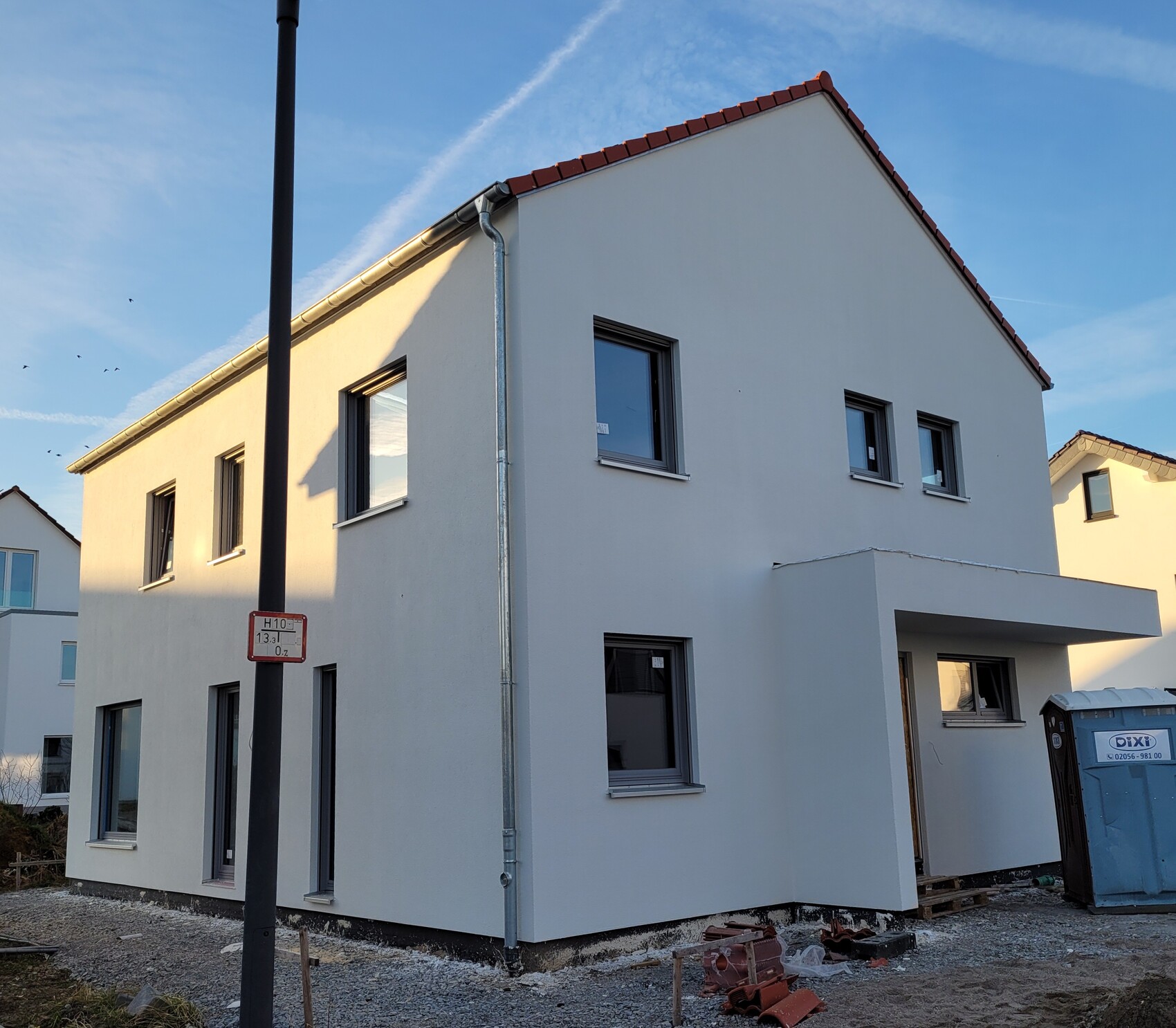Hellgraues zweigeschossiges Haus im Rohbauzustand mit grauer Fassade und rotem Dach